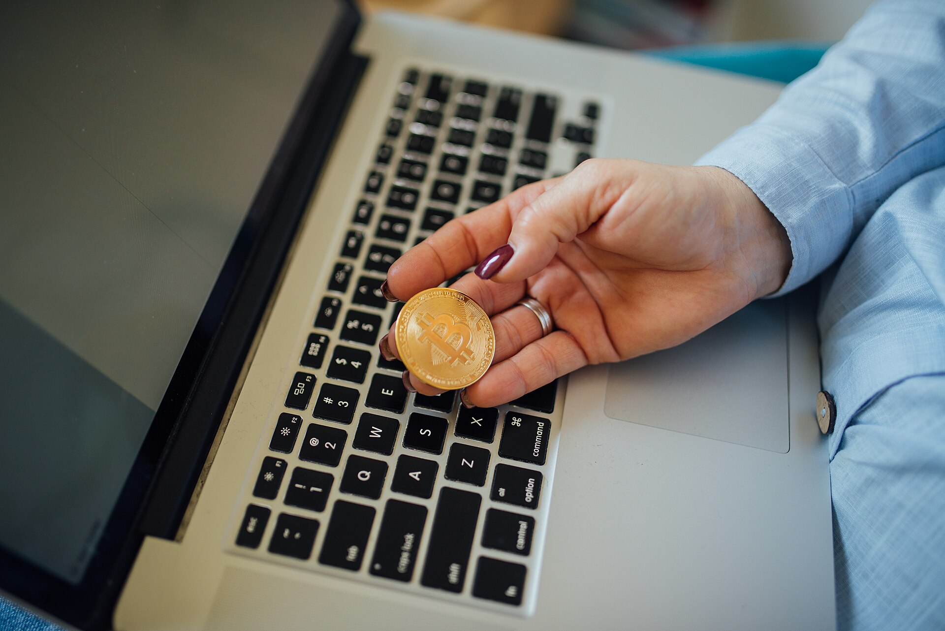 A physical Bitcoin token held in a hand next to a laptop, illustrating cryptocurrency trading