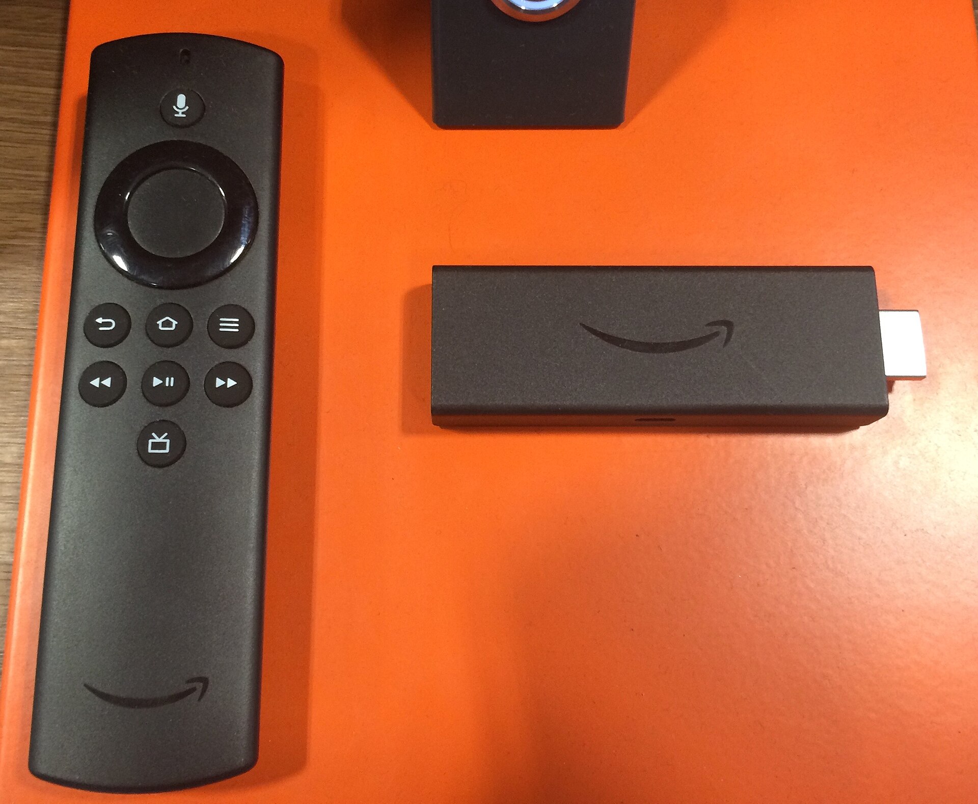 An Amazon Fire TV Stick plugged in beside its voice remote